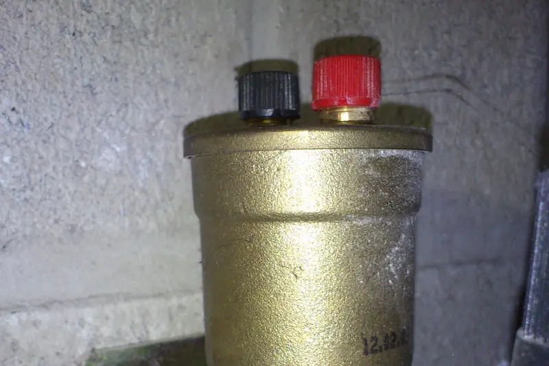 Brass automatic air vent topped with a black cap and a red cap, threaded into a brass pipe fitting