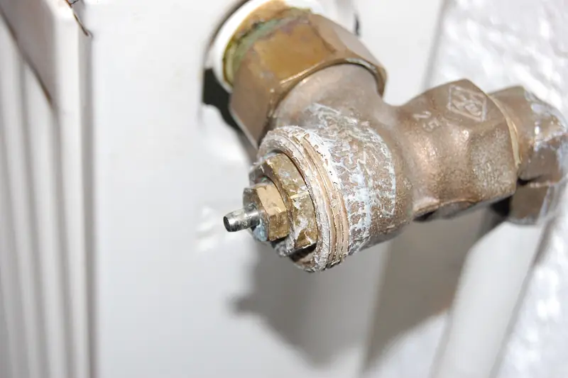 Close view of a worn brass radiator valve, paint flaking around its bare spindle