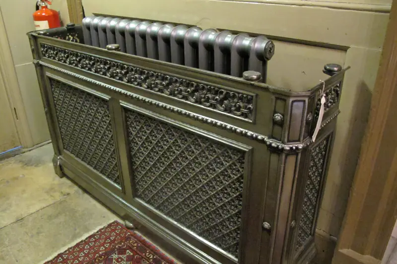 Antique metal radiator cabinet with pierced fretwork panels on the front and sides, the tops of the cast-iron columns showing above it